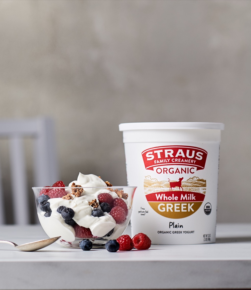 Straus Whole Milk Greek Yogurt tub beside a berry and granola yogurt bowl