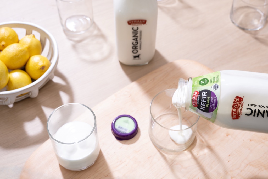 Pouring Straus Organic Plain Kefir into a glass beside a basket of lemons
