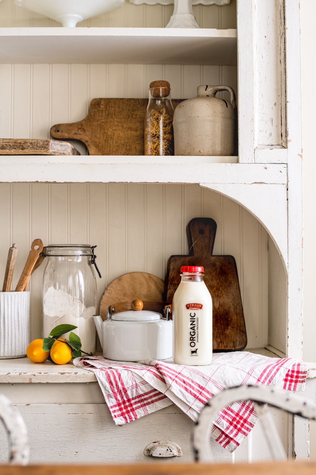 Glass Straus Organic milk bottle on a farmhouse hutch with lemons and a white enamel kettle