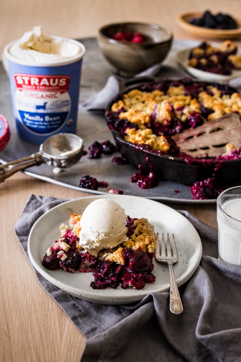 Scoop of Straus Vanilla Bean ice cream melting over a plate of berry crumble beside the pint