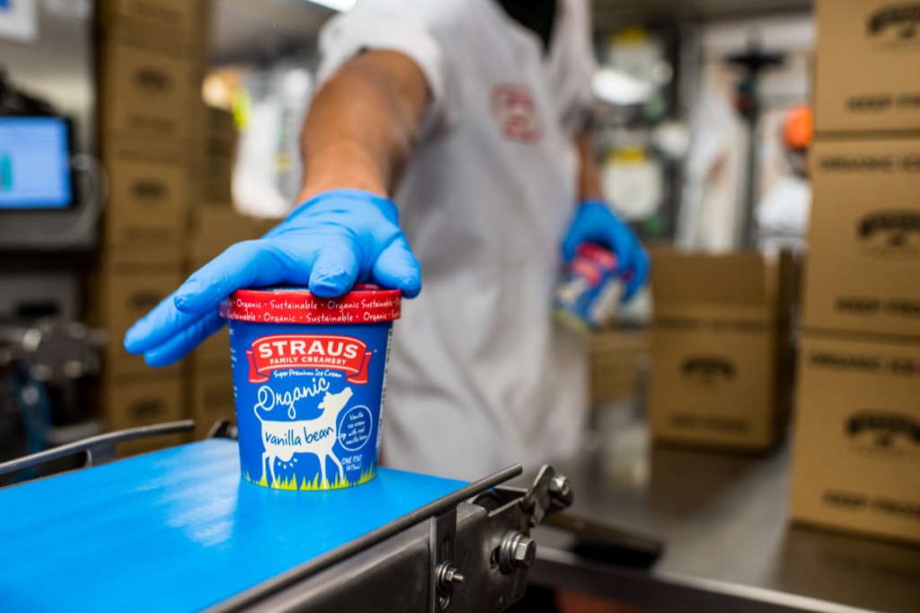 Gloved worker placing a Straus Family Creamery Organic Vanilla Bean ice cream pint on the production line