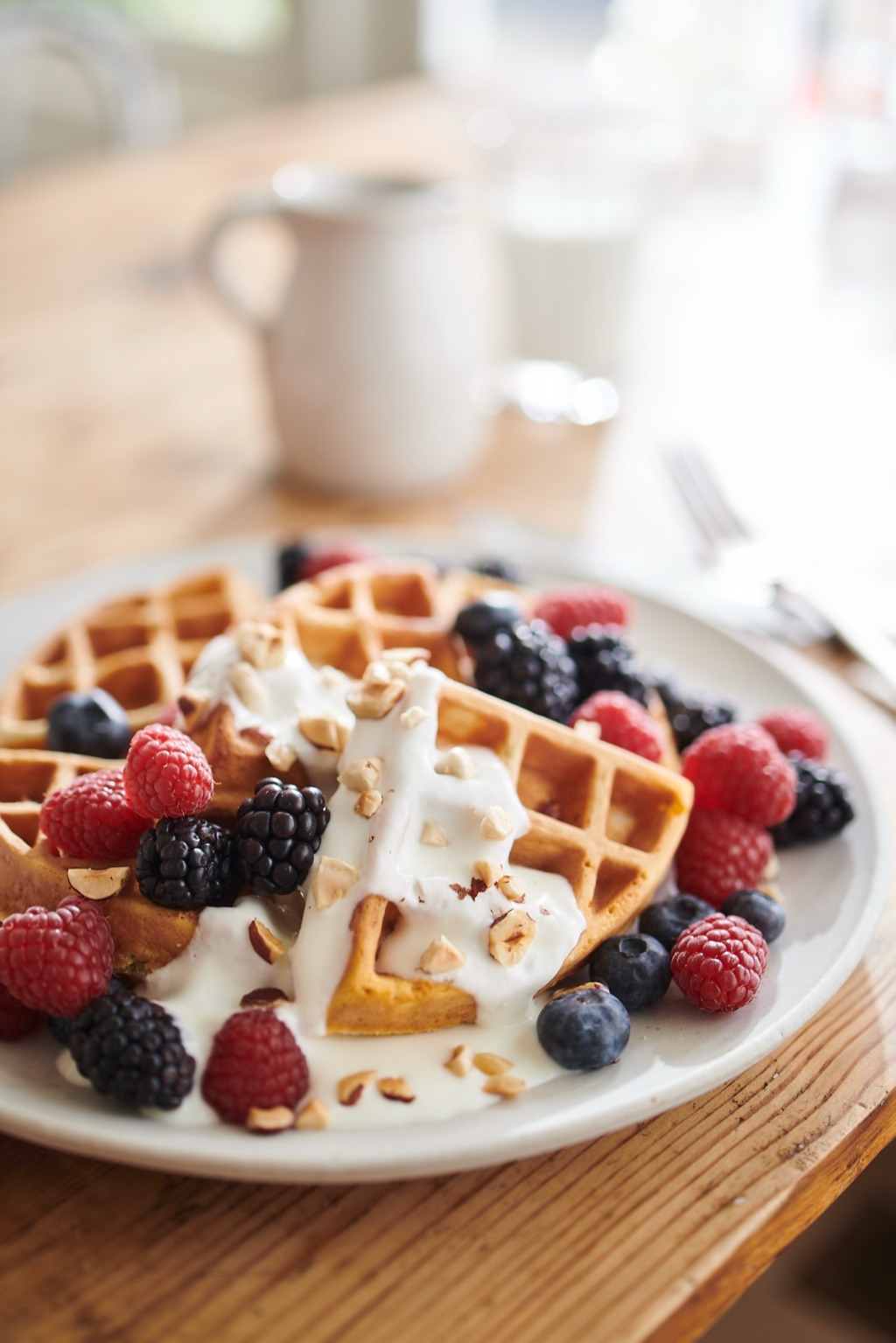 Waffles topped with yogurt, fresh berries, and chopped hazelnuts in soft window light