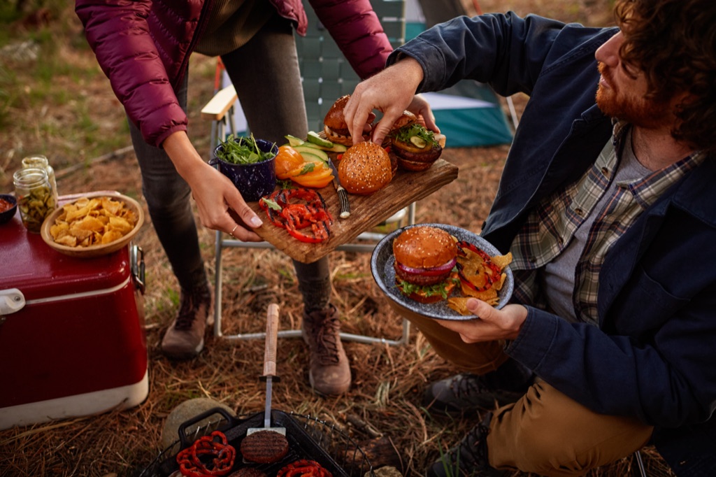 Camper passing a board of Awesome Burgers with grilled peppers and avocado while a friend holds his plate