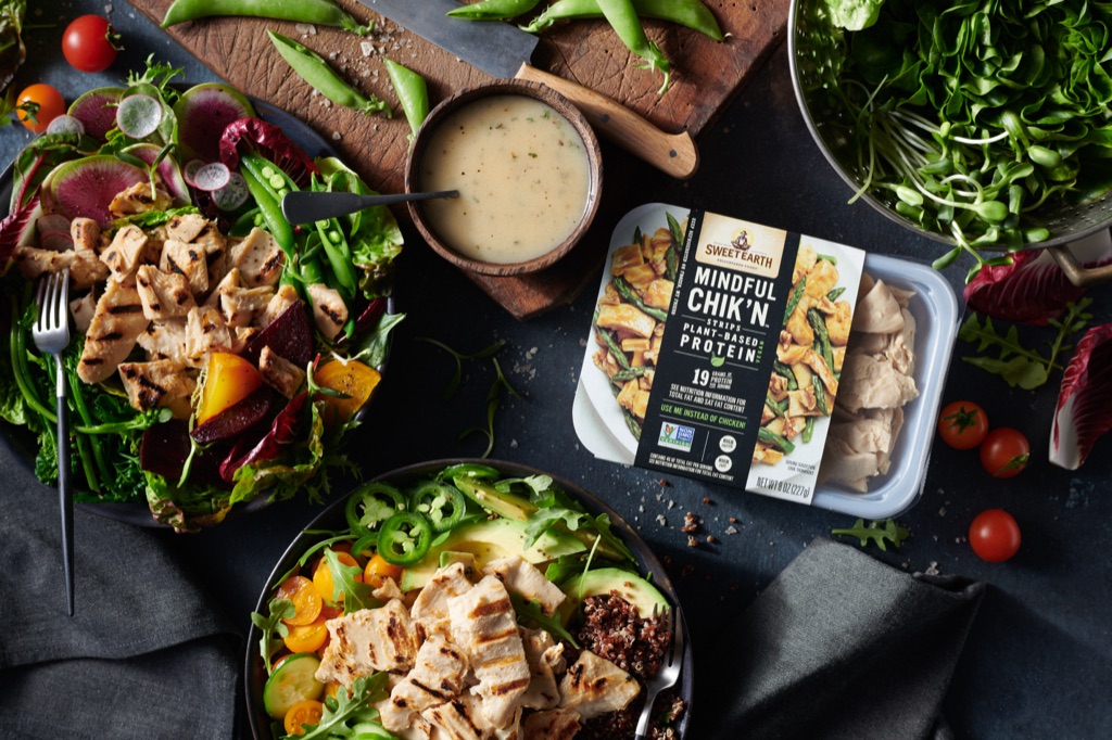 Sweet Earth Mindful Chik'n package styled with fresh salads, herb dressing, and greens on a dark tabletop