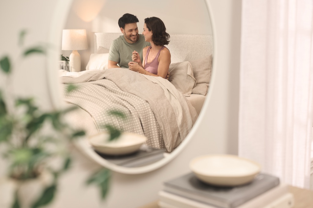 Couple laughing together in bed, seen through a round mirror, photographed for Tempur-Sealy by Dawn Heumann
