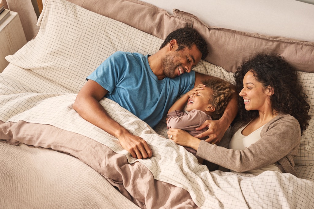 Parents cuddling their giggling child between them in bed, Sealy campaign lifestyle photography