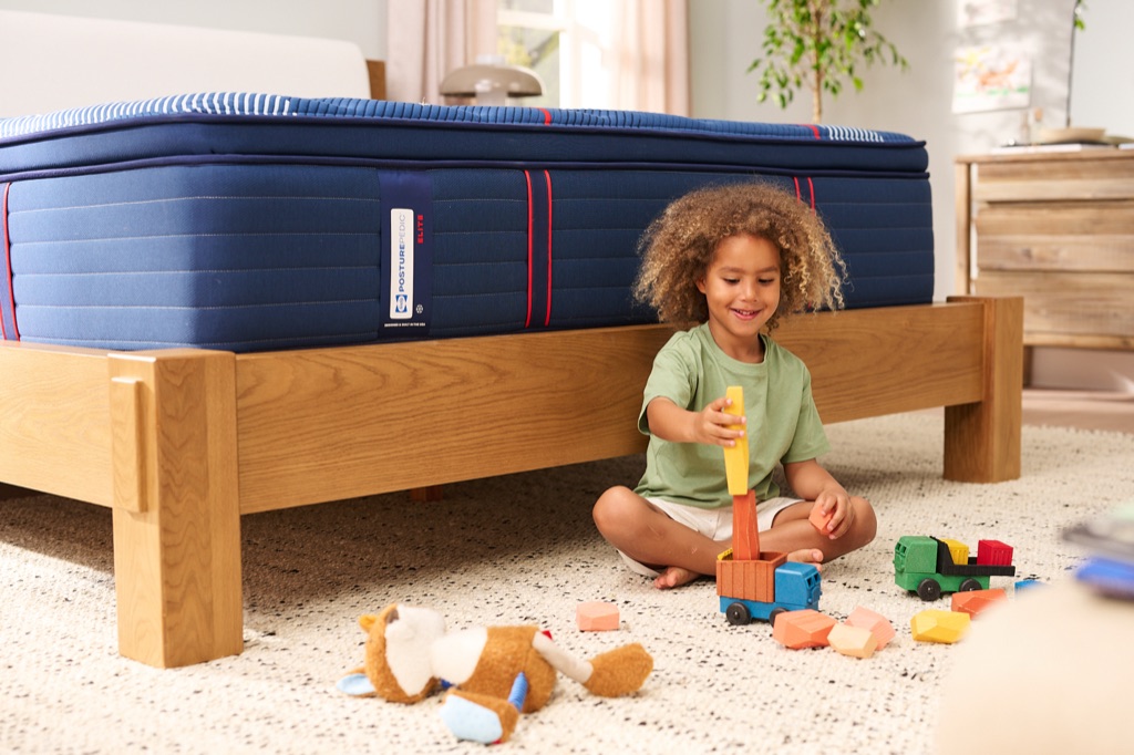Child playing with wooden blocks on the floor beside a Sealy Posturepedic Elite mattress