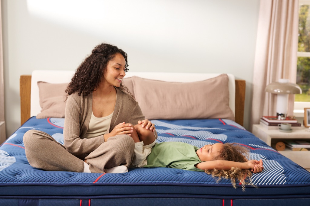 Mother sitting cross-legged while her child stretches out on a Sealy Posturepedic Elite mattress