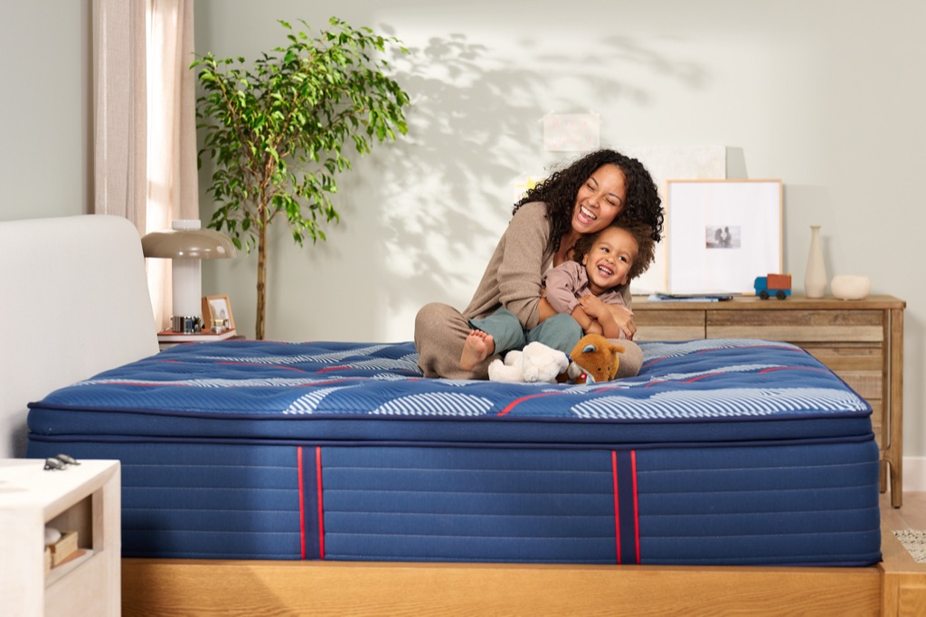 Mother hugging her laughing toddler on a Sealy Posturepedic Elite pillow-top mattress with stuffed animals, photographed by Dawn Heumann