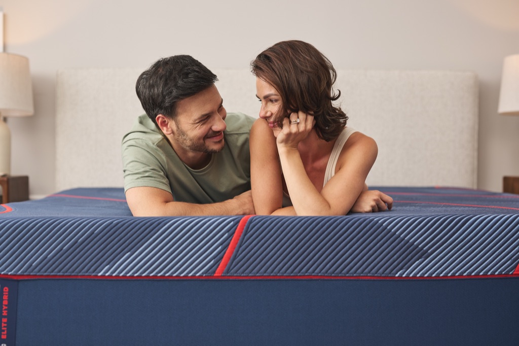 Couple smiling at each other at the foot of a Sealy Posturepedic Elite Hybrid mattress