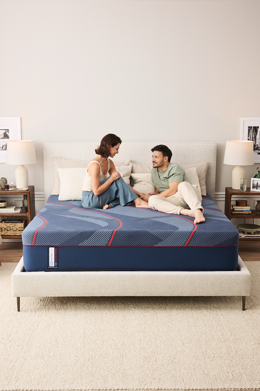 Couple sitting and talking on a Sealy Posturepedic Elite Hybrid mattress, full bedroom view
