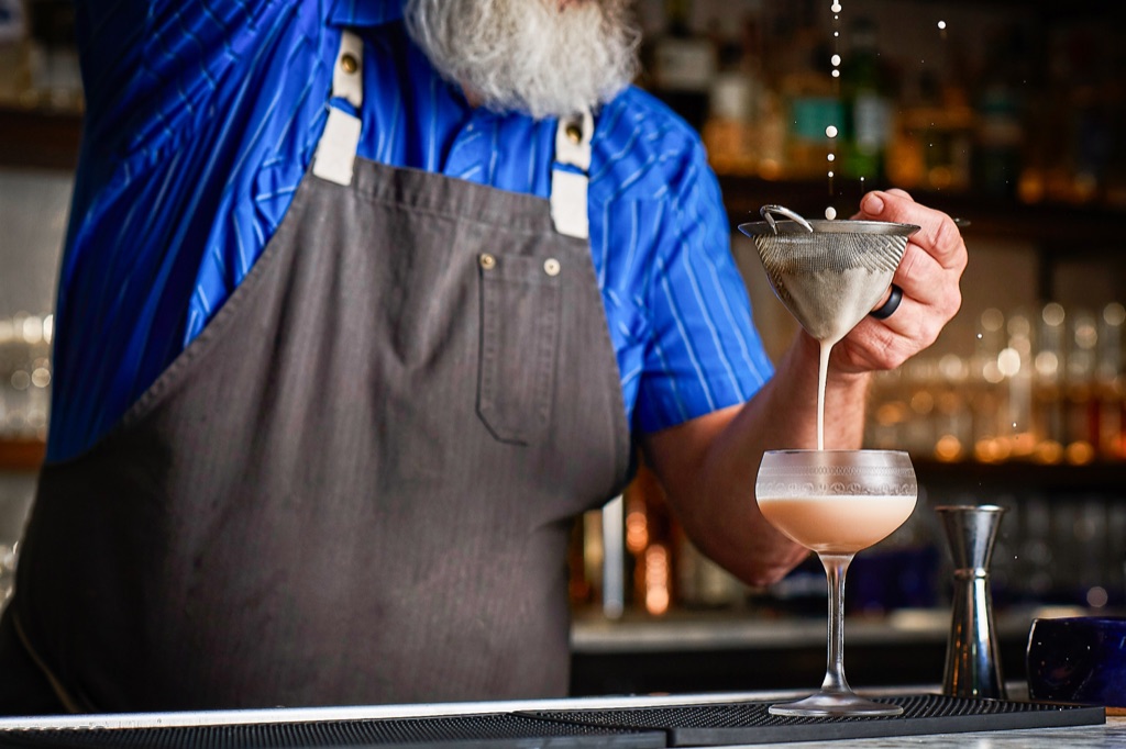 Bartender fine straining a cocktail into a coupe at the bar, photographed by Dawn Heumann