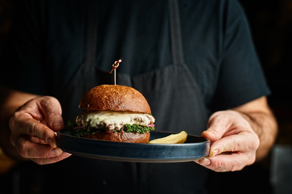 Hands holding a cheeseburger in moody restaurant light