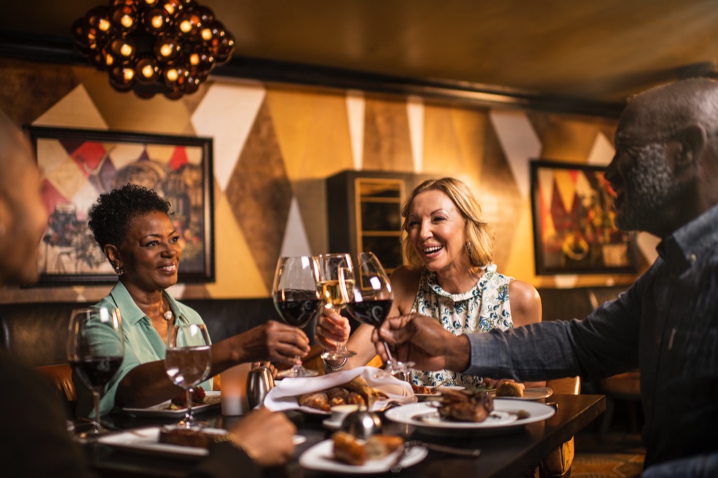 Two couples toasting red and white wine in a warm steakhouse