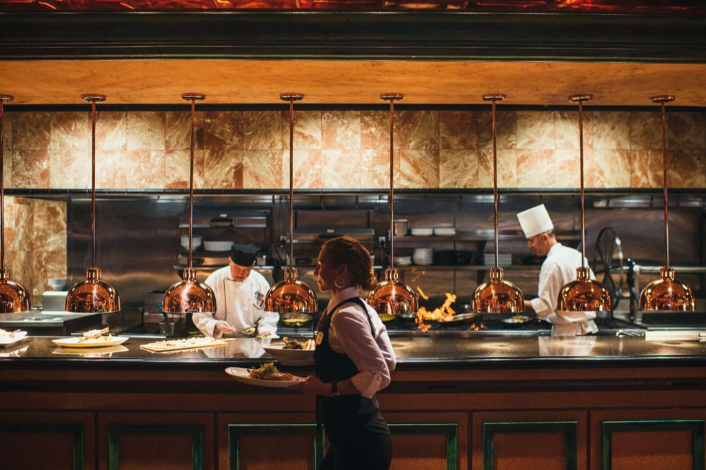 Open restaurant kitchen glowing under copper pendant lamps during service