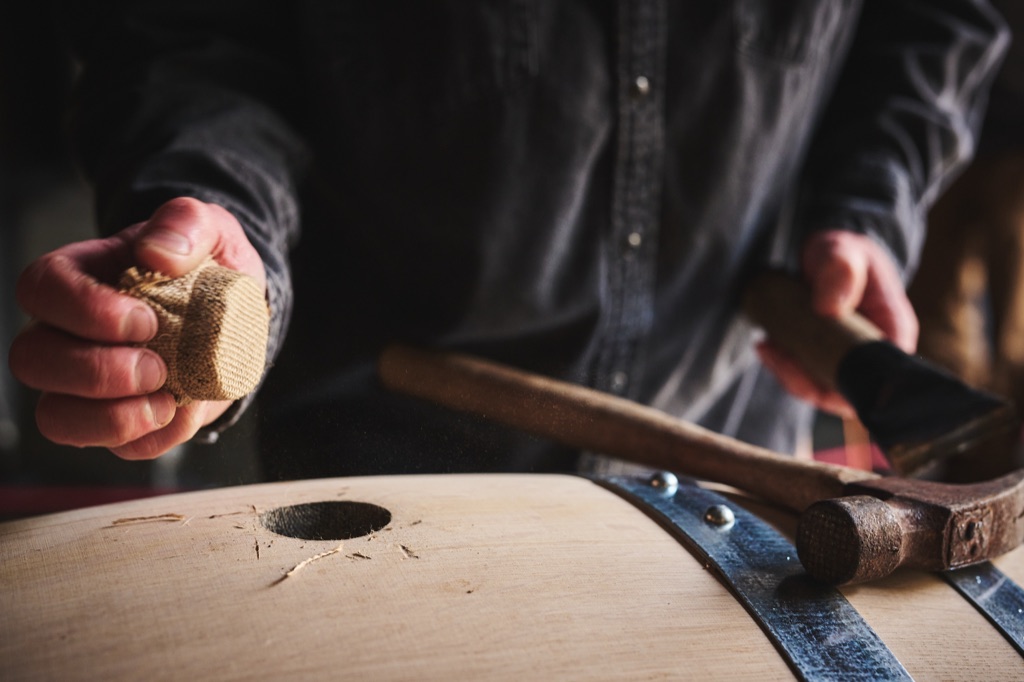 Cooper's hands setting a burlap-wrapped bung into a new oak barrel