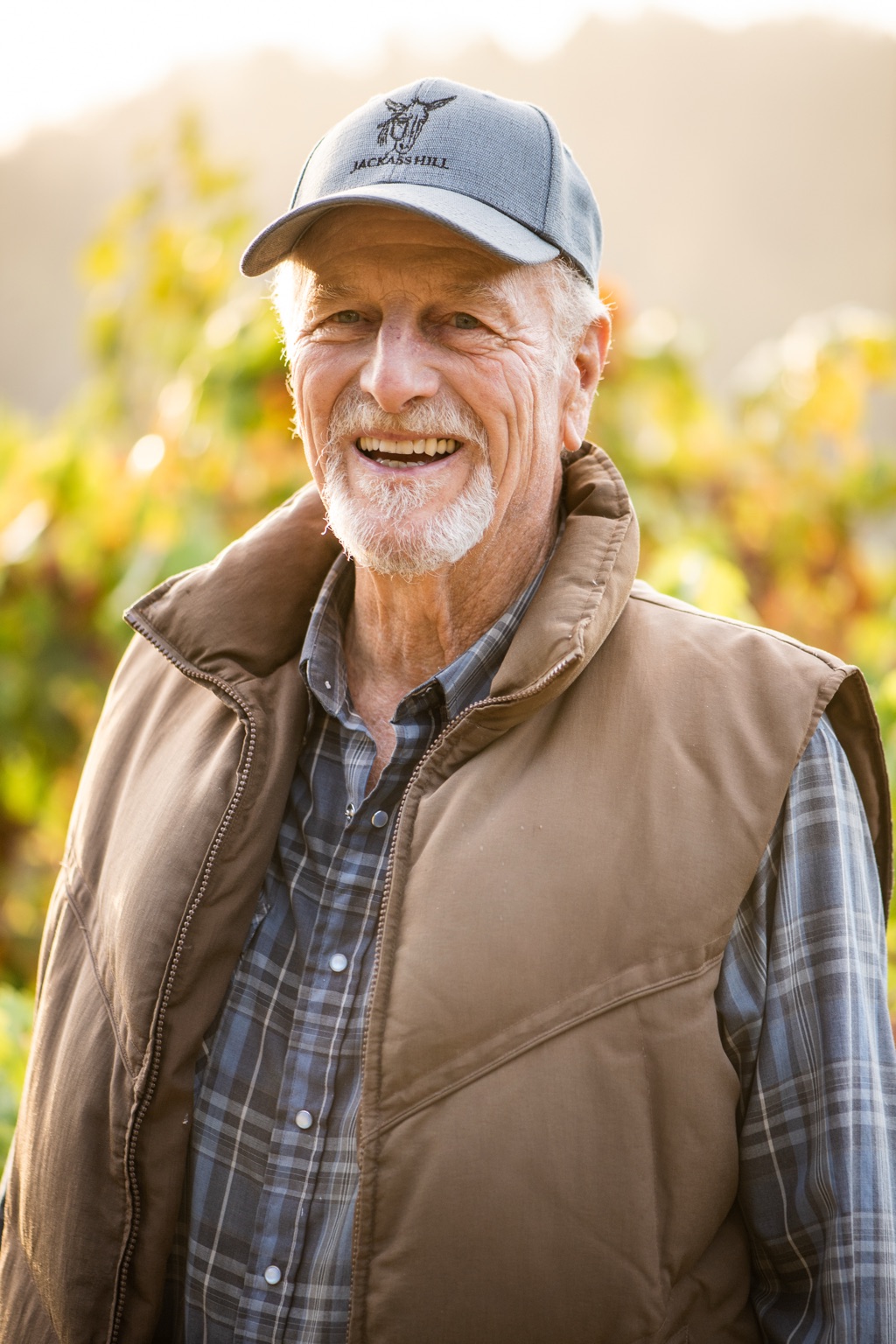 Portrait of a smiling grower in a Jackass Hill cap among turning autumn vines