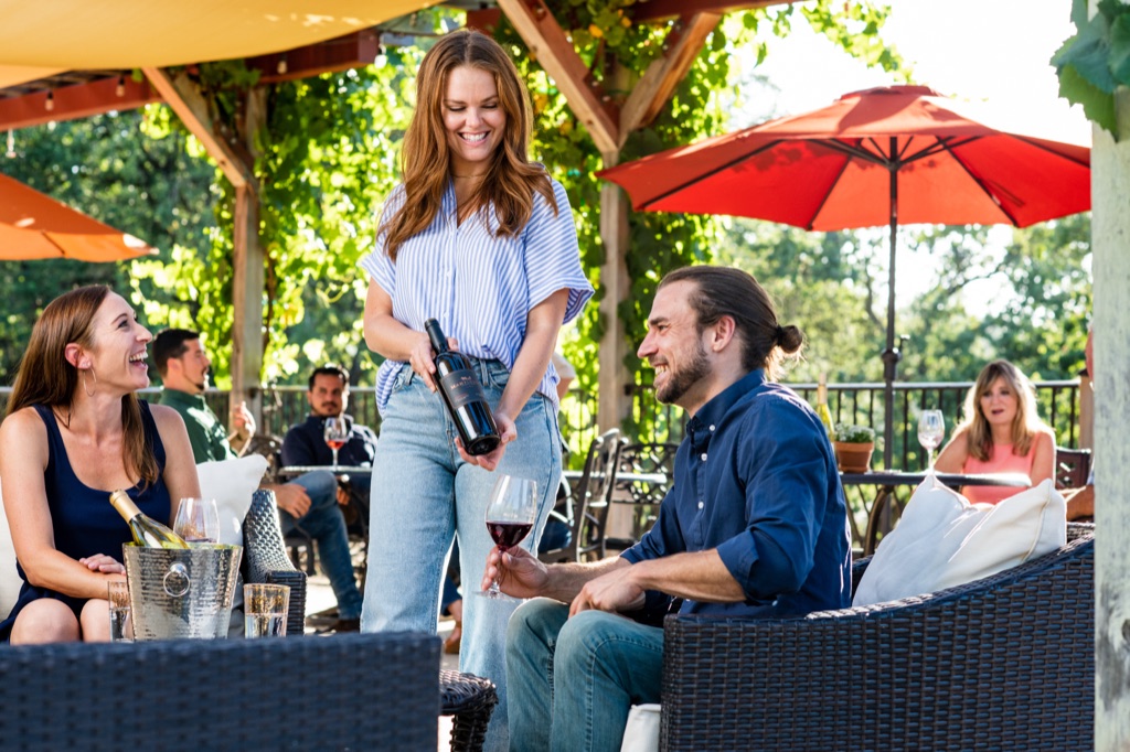 Host presenting a Martinelli red to a couple relaxing on the winery's umbrella-shaded patio