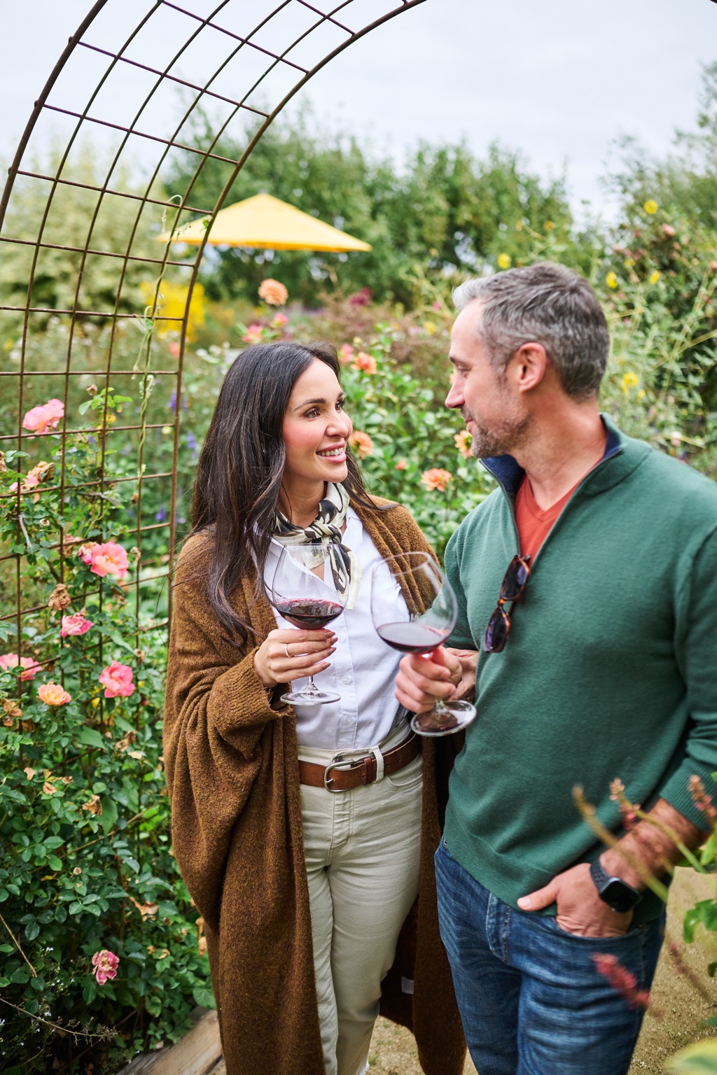 Couple sharing red wine under a climbing rose arbor in a winery garden