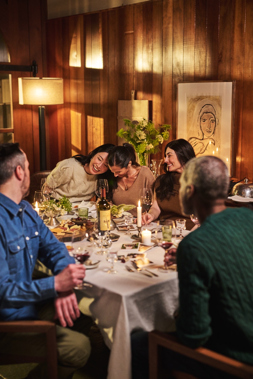 Candlelit dinner party with friends laughing around a wood paneled dining room