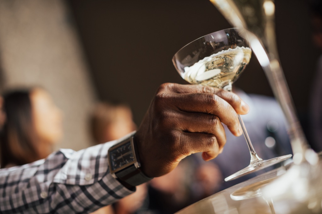 Hand raising a coupe of sparkling wine at the bar in warm light