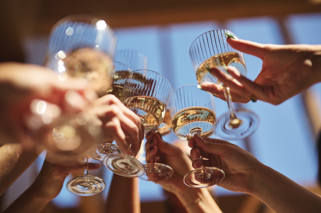 Hands clinking ribbed coupes of white wine against a bright sky