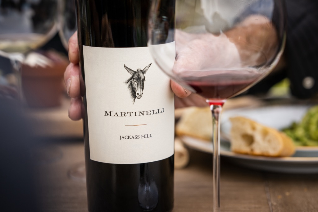 Bottle of Martinelli Jackass Hill held beside a glass of red at an outdoor lunch