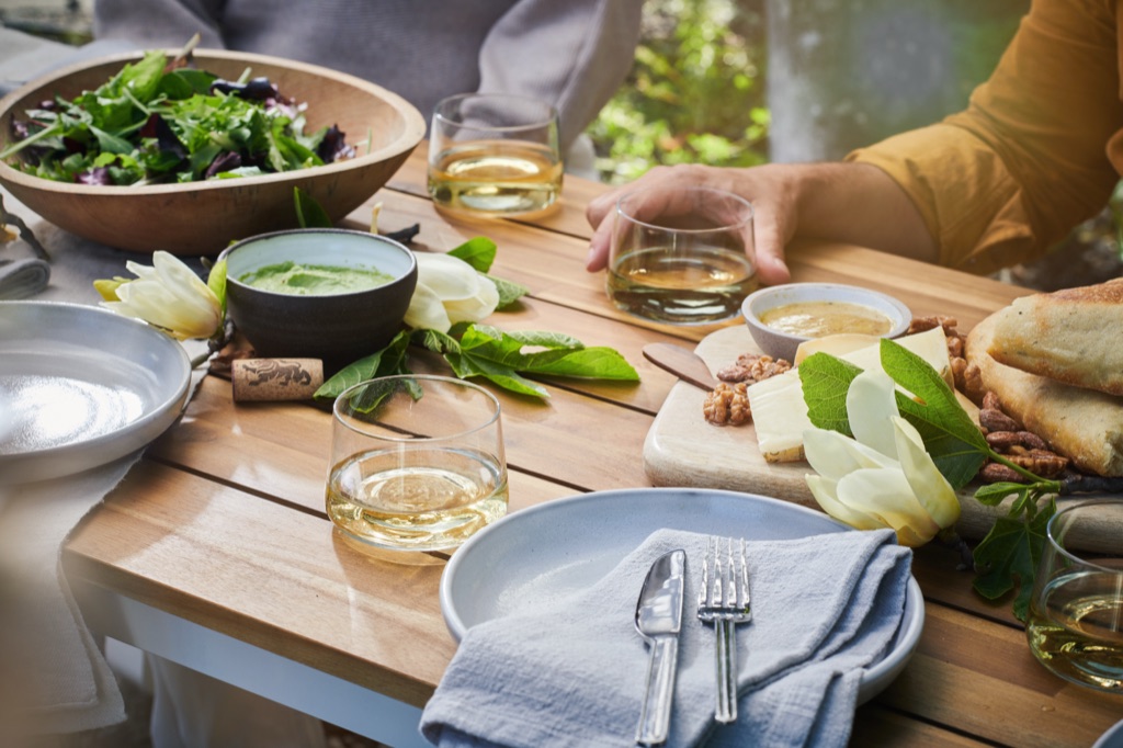 White wine in stemless glasses at a shaded outdoor lunch with a cheese board and magnolia blossoms