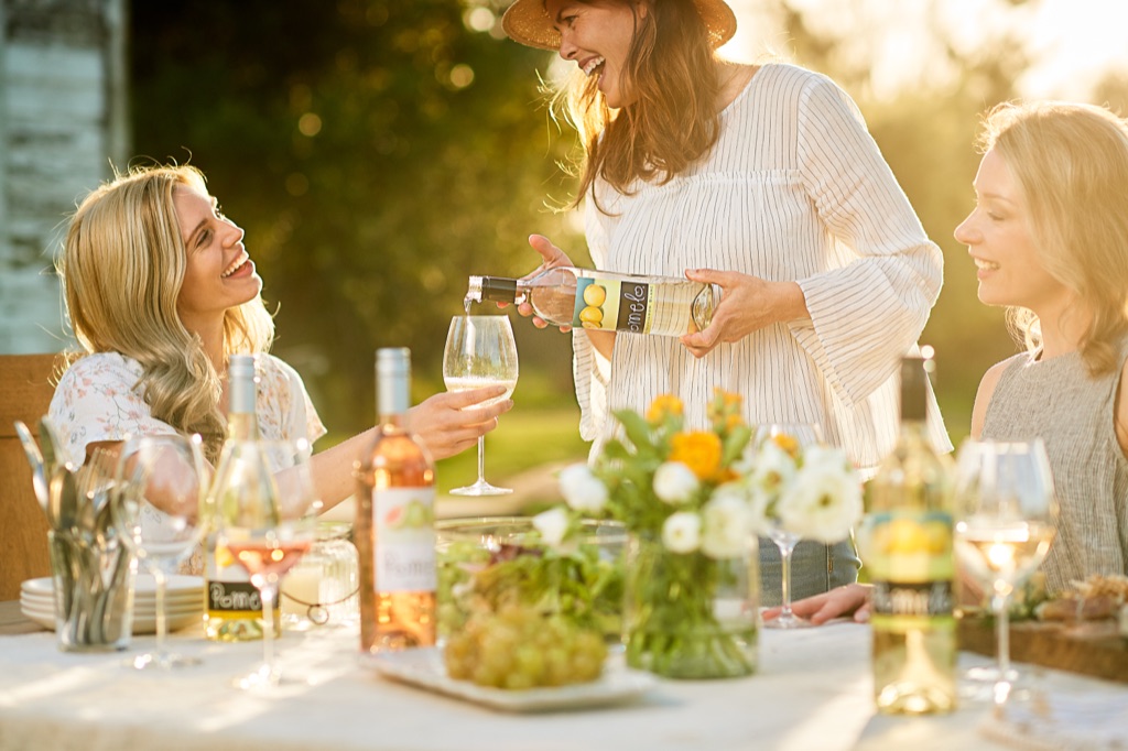 Women laughing at a golden hour garden party as the host pours Pomelo sauvignon blanc