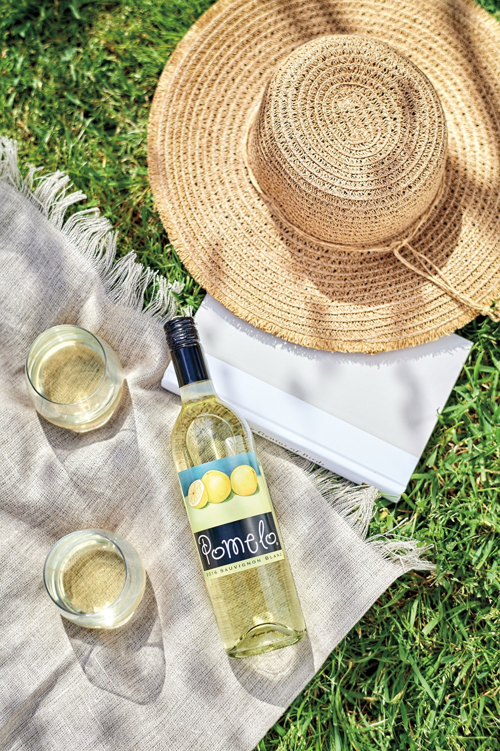 Pomelo sauvignon blanc picnic flat lay with a straw hat, book, and linen blanket