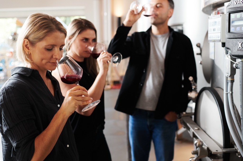 Three people tasting young red wine straight from the tank in a winery
