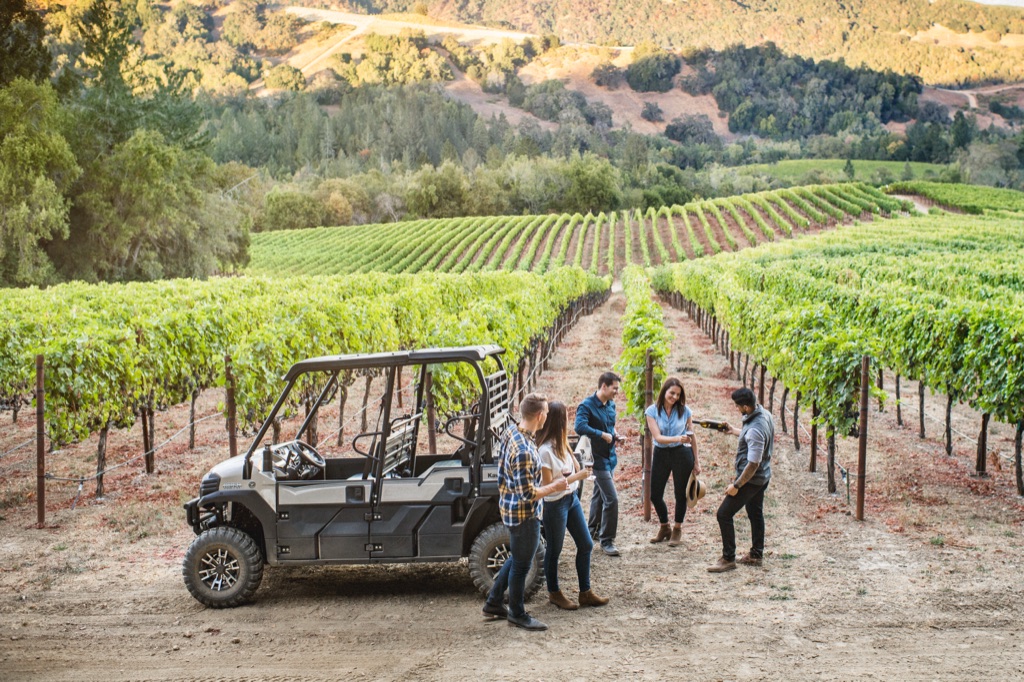 Friends wine tasting beside a UTV between vineyard rows in golden evening light