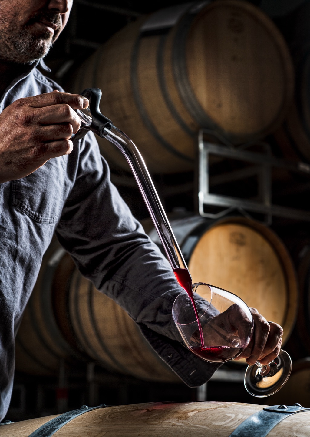 Winemaker filling a glass of red from the barrel with a wine thief in the barrel room