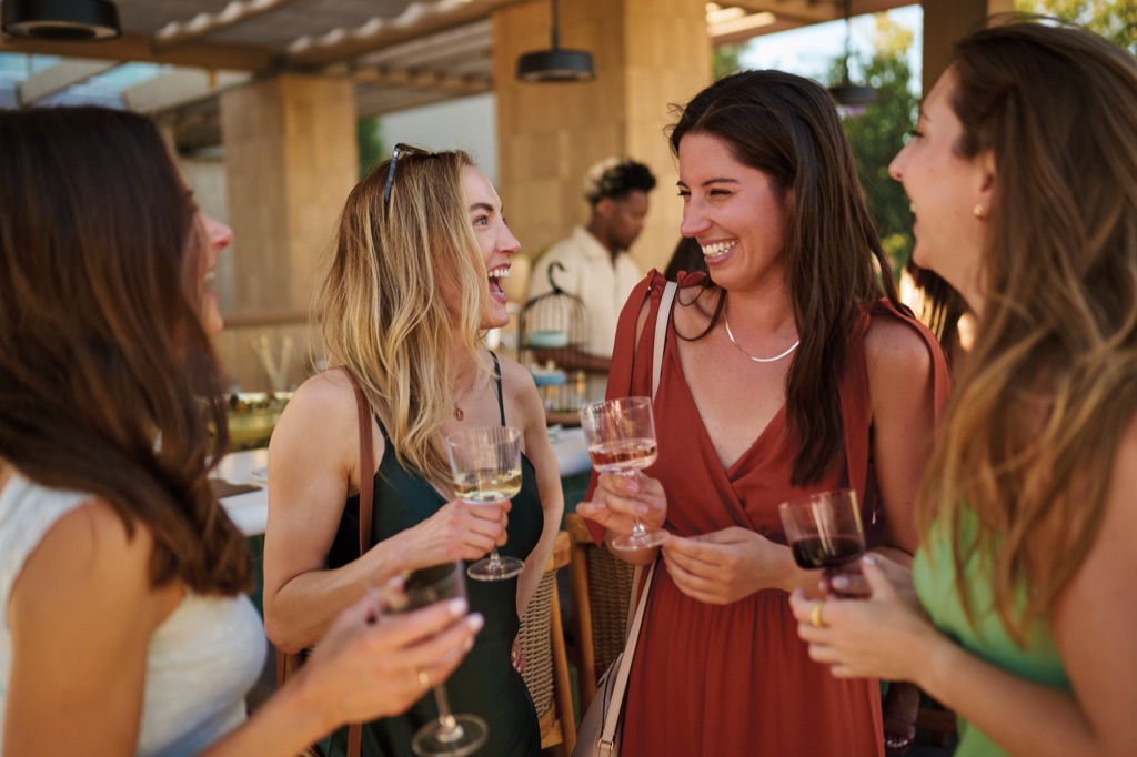 Four women laughing over wine glasses at an outdoor winery bar